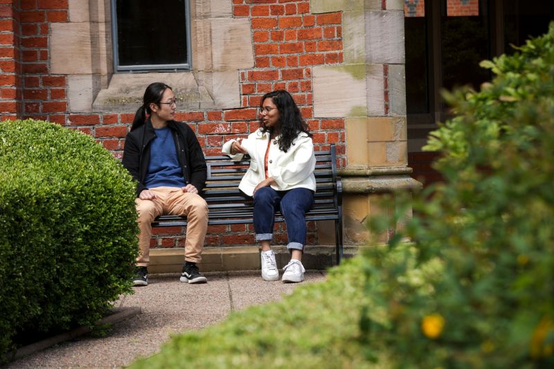 male student and female student sitting chatting on bench in the Lanyon area of Queen's